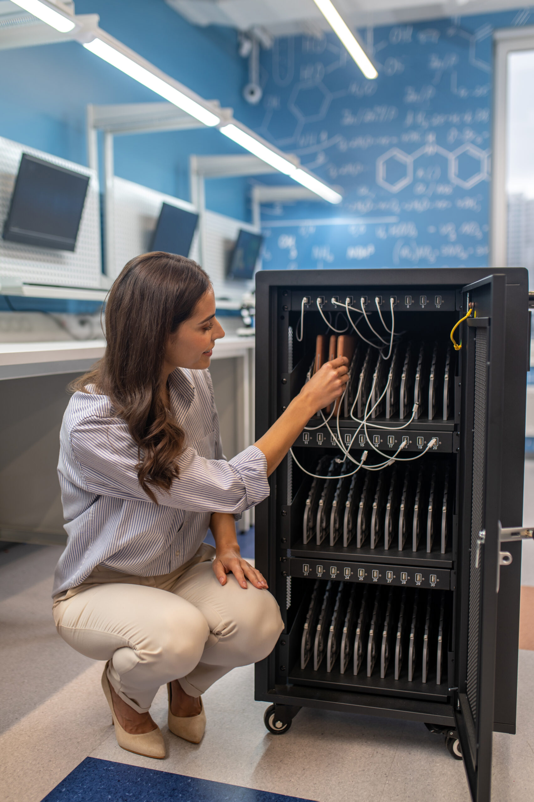 Charging board. Woman crouching near open special cabinet with wires touching charging boards in chemistry class